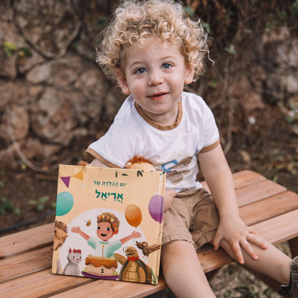 Child sitting on a wooden bench holding a colorful book outdoors.